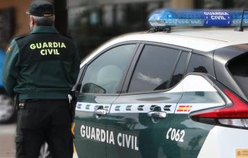 Un agente de la Guardia Civil, de espaldas, de pie junto a un vehículo oficial