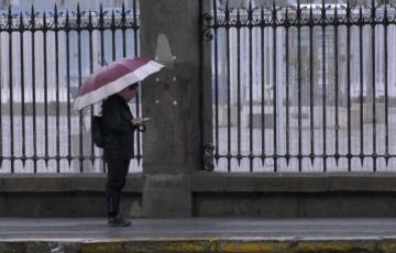 Un viandante se protege de las inclemencias junto a la veja del muelle en la capital gaditana