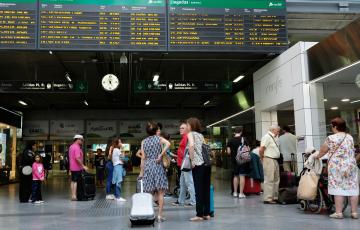 Viajeros esperando frente a uno de los paneles de salidas y llegadas de una estación de trenes.