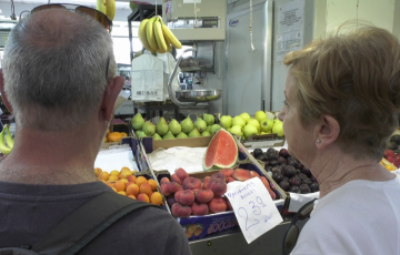 Clientes del Mercado Central junto a un puesto de frutas y verduras. 