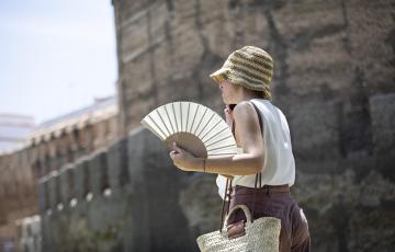 Una mujer se protege de las altas temperaturas con sombrero y abanico.