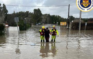 Dos bomberos ayudan a una persona en Arcos a salir de la zona inundada con motivo de la crecida del agua por la apertura de la presa