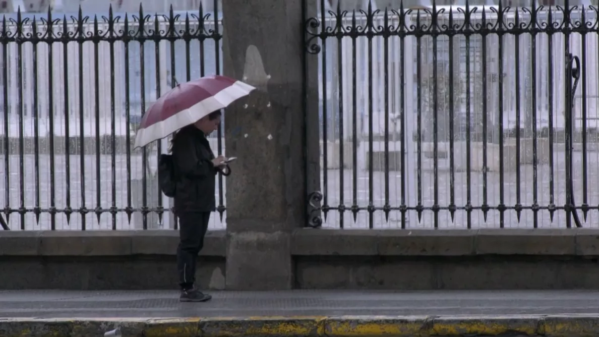 Un viandante se protege de las inclemencias junto a la veja del muelle en la capital gaditana
