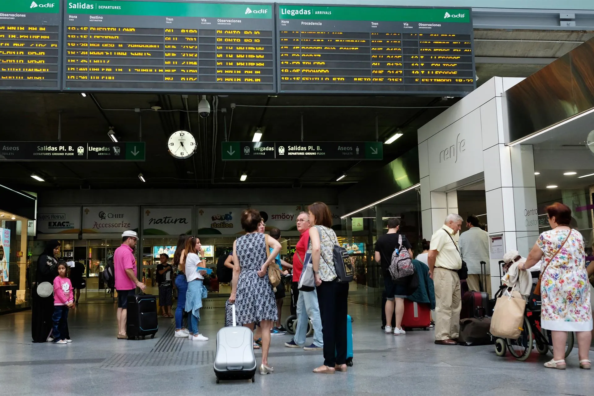 Viajeros esperando frente a uno de los paneles de salidas y llegadas de una estación de trenes.