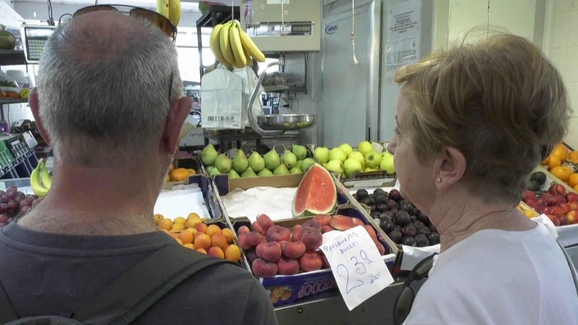 Clientes del Mercado Central junto a un puesto de frutas y verduras. 