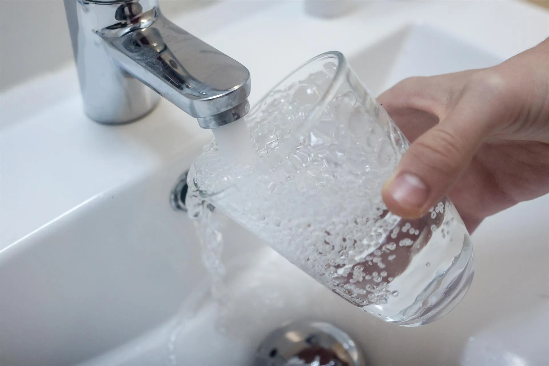 Una persona llena un vaso de agua de un grifo.